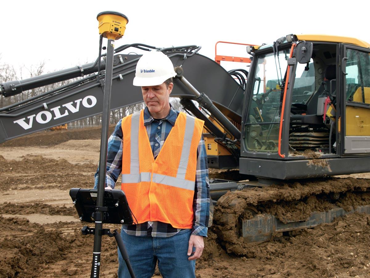 Man in PPE using Machine Guidance with excavator in background